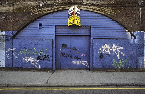 vodoravna fotografija obokanega vhoda , z modro prepleskano fasado z grafiti, modrimi vrati in napisom nad vhodom
