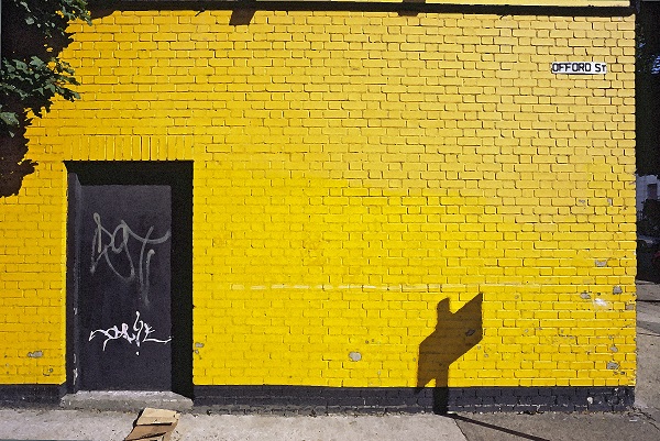vodoravna fotografija dela stavbe v Londonu, s prepleskano rumeno fasado, brick wall in črnimi vrati